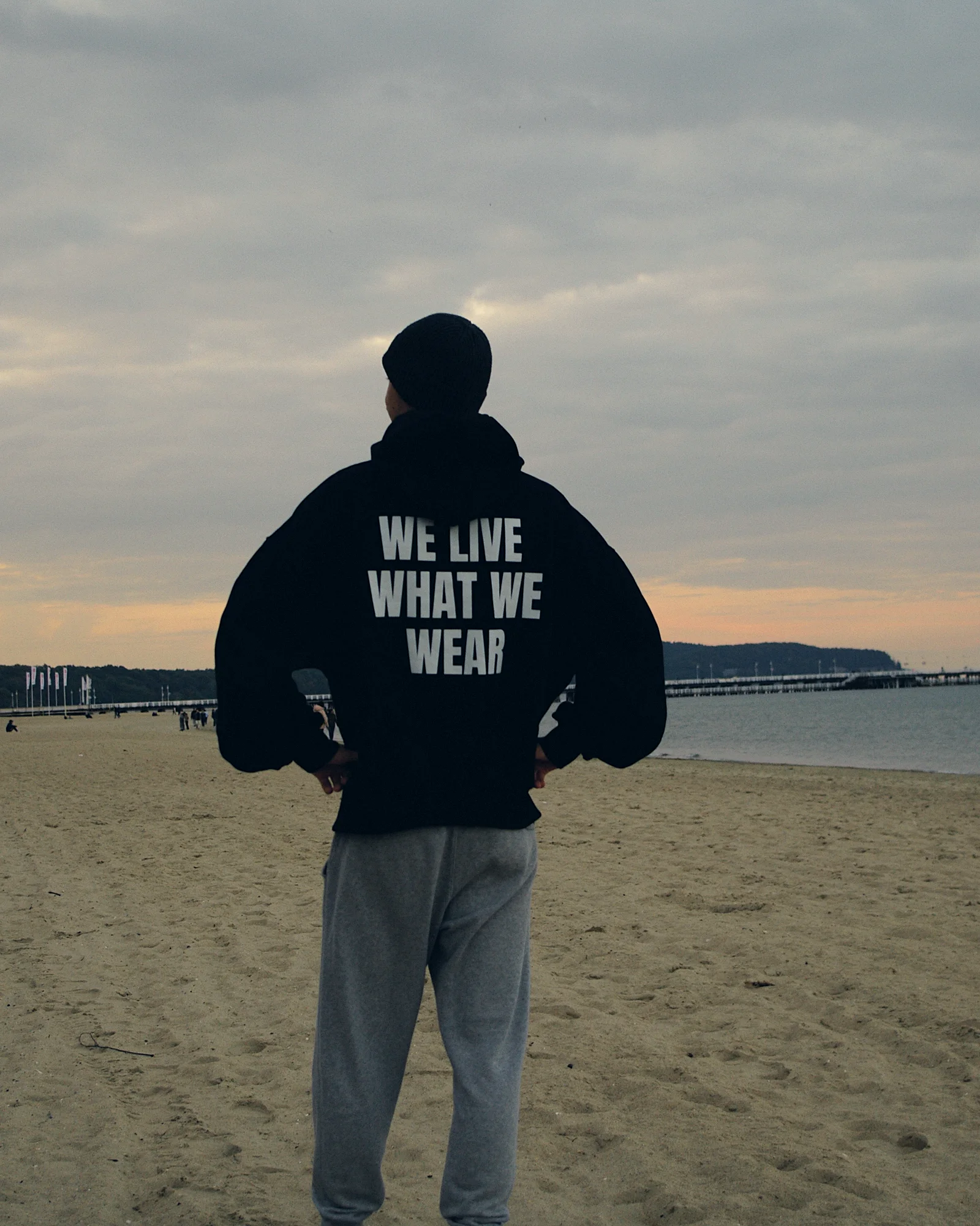 Plaża w Sopocie o zmierzchu, postać w bluzie ROKE tyłem, na plecach WE LIVE WHAT WE WEAR