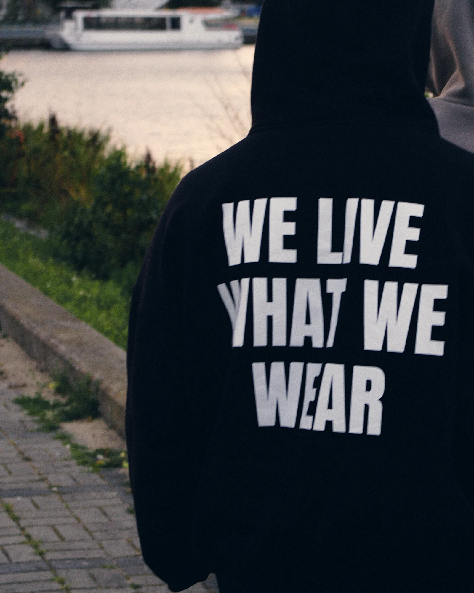 Plecy z nadrukiem WE LIVE WHAT WE WEAR, zielona ścieżka nad wodą